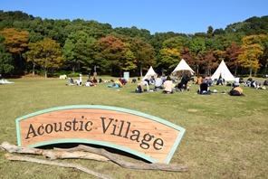 Acoustic Villageの看板と野外でヨガを楽しむ人々
