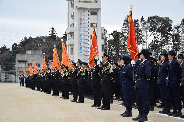 整列し旗を掲げる消防職員と消防団員