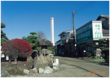 青空の下に、紅葉したつつじとともに納まる白い煙突の写真